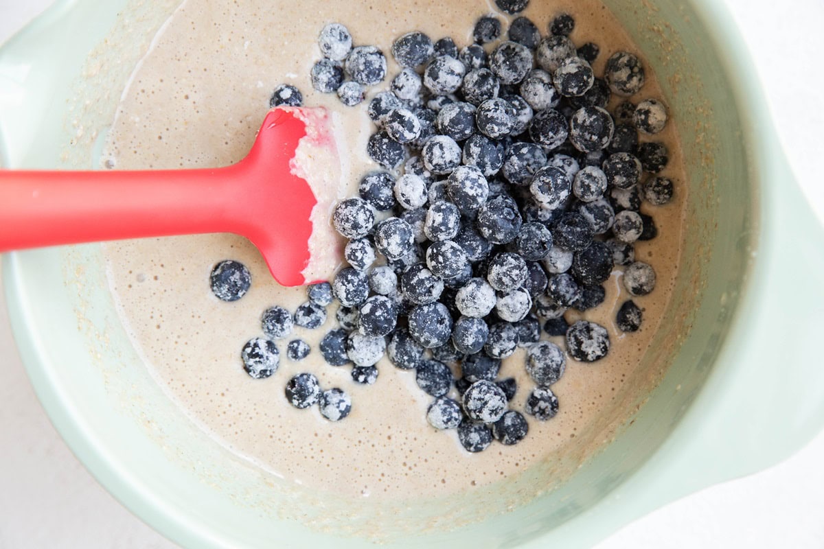 Mixing bowl with muffin batter and blueberries on top, ready to be mixed in.