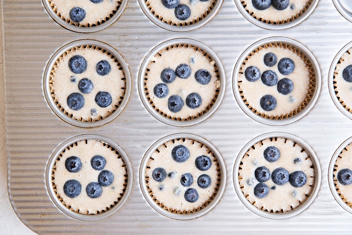 Muffin pan with blueberry muffin batter inside, ready to go into the oven.