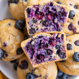 White plate with blueberry muffins and one sliced in half, exposing the blueberry inside.