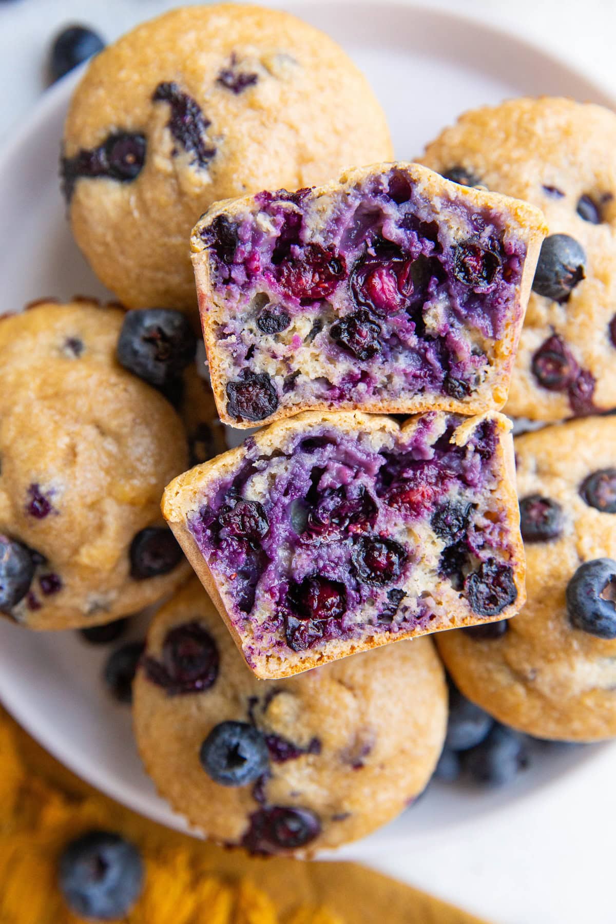 White plate with blueberry muffins and one sliced in half, exposing the blueberry inside.