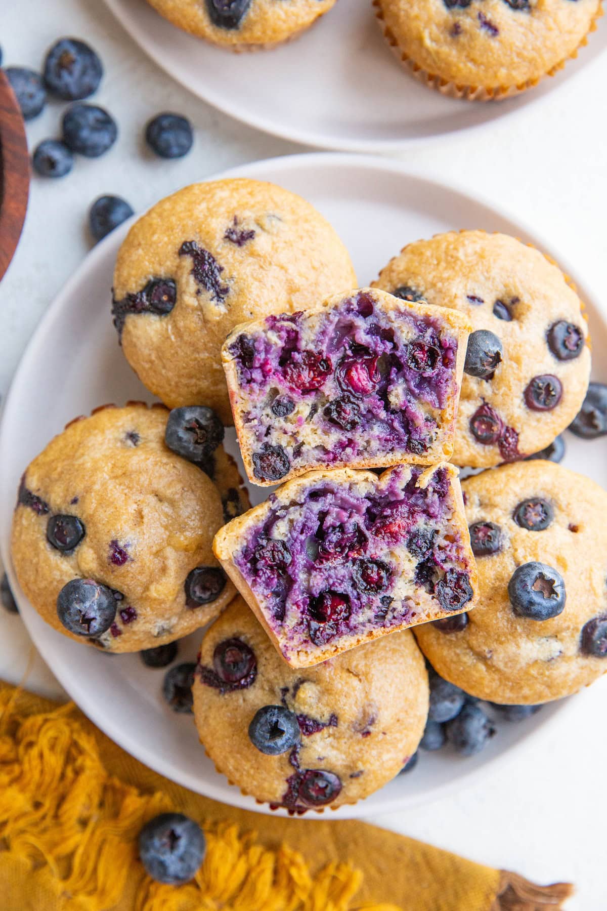 White plate of blueberry muffins with one sliced in half, exposing the inside.