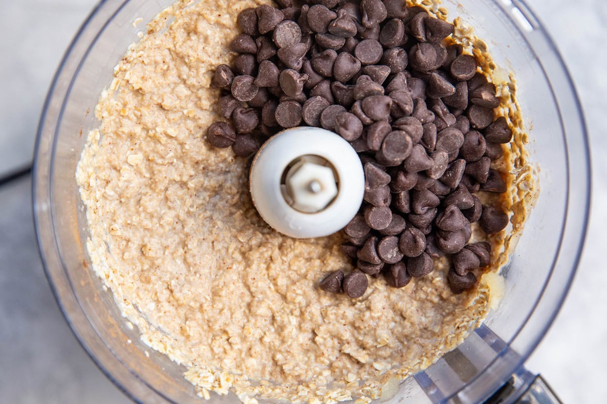 Ingredients for oatmeal applesauce bars in a food processor with chocolate chips on top, ready to be mixed in.