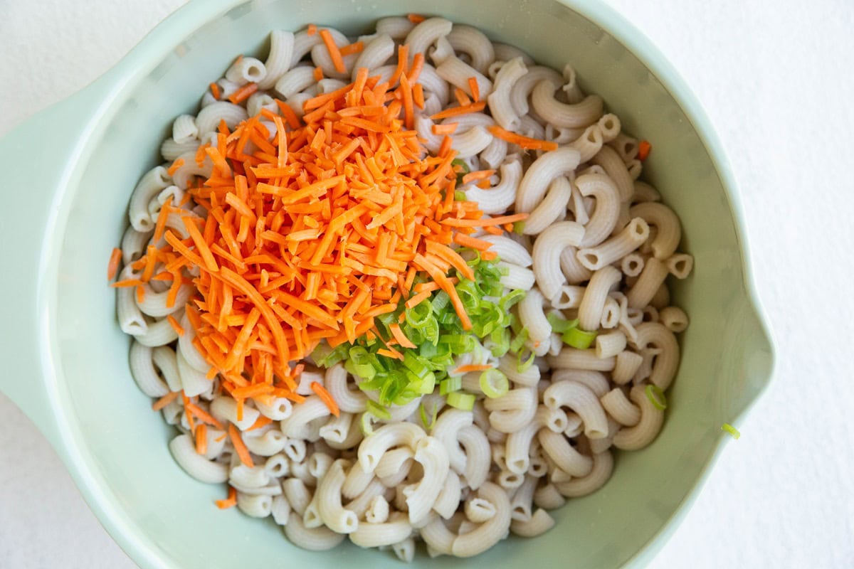 Mixing bowl with cooked noodles, carrots, and onions.