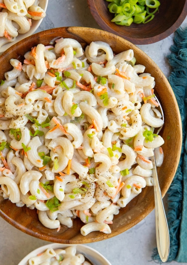 Wooden bowl of macaroni salad with bowls of macaroni salad to the side.