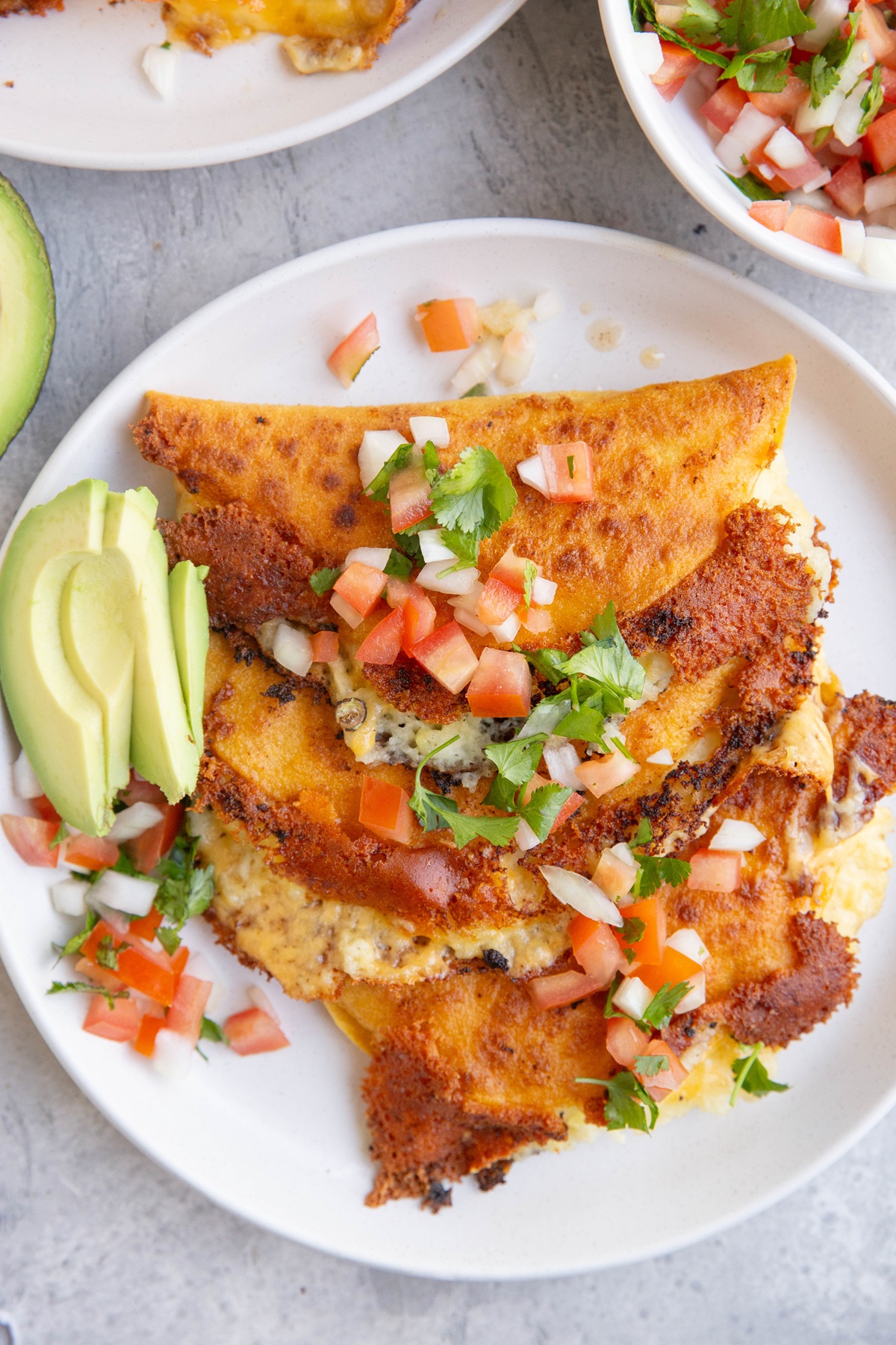 Crispy cheesy potato tacos on a plate with slices of avocado and homemade pico de gallo