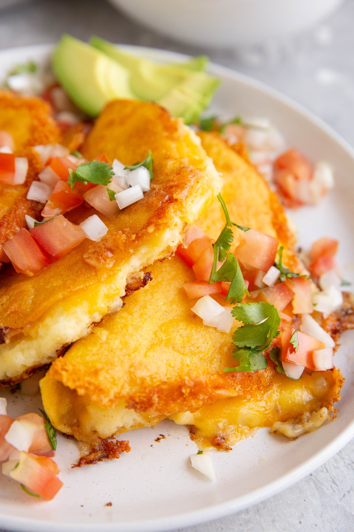 White plate of crispy potato tacos with pico de gallo on top, ready to eat