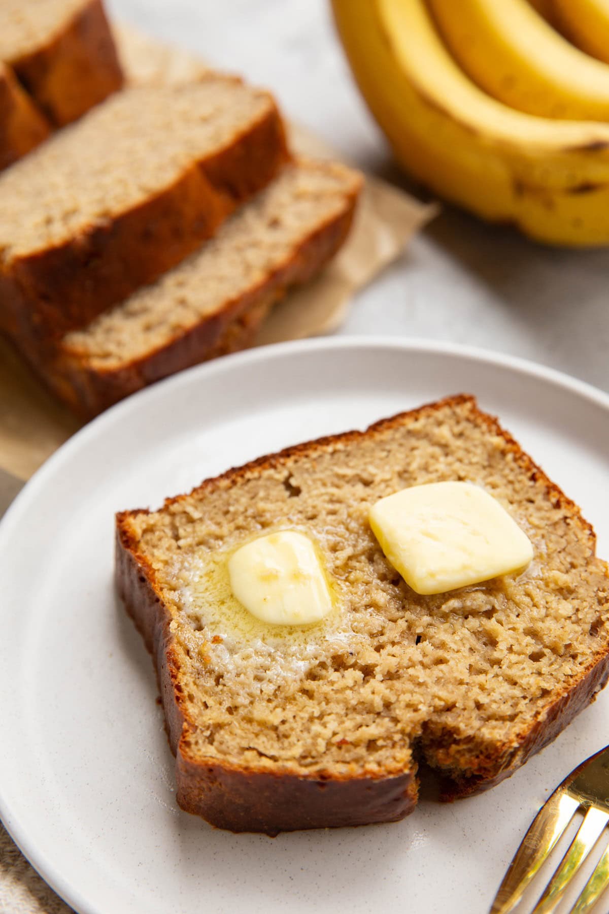 Slice of banana bread on a white plate with melted butter on top.