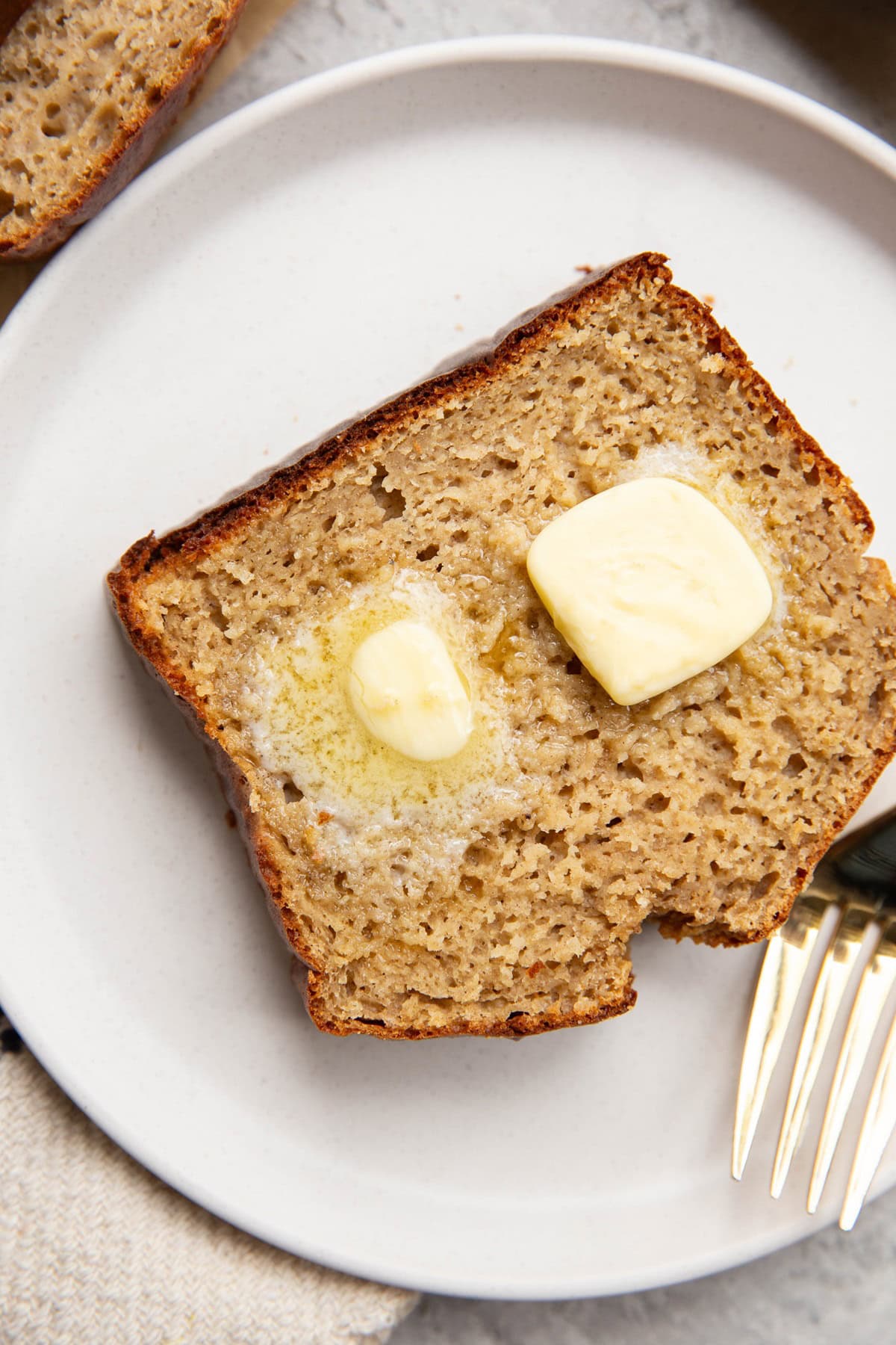 Thick slice of banana bread on a white plate with melted butter on top, ready to eat.