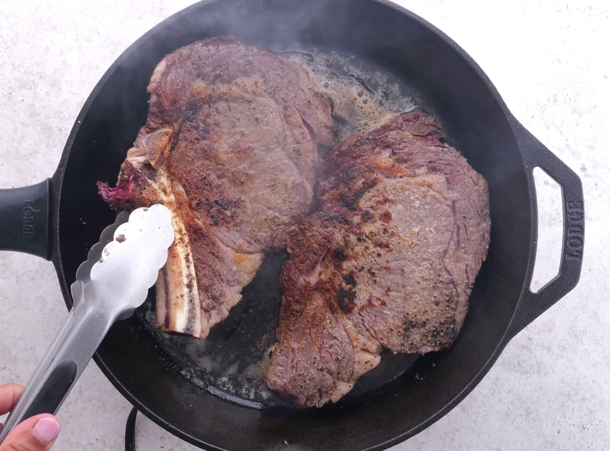 Flipping steaks over using tongs.