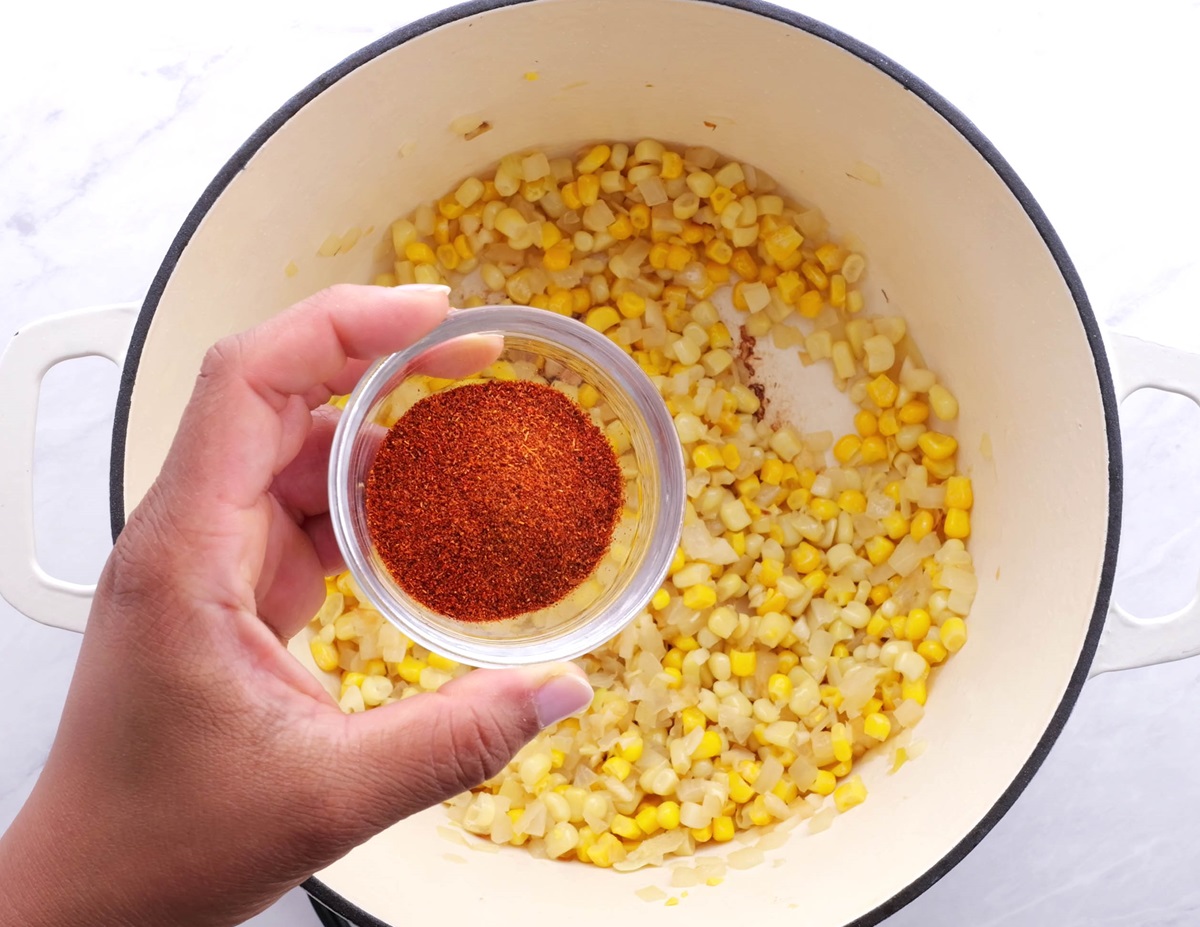 Corn and onion cooking in a pot with paprika being added in.