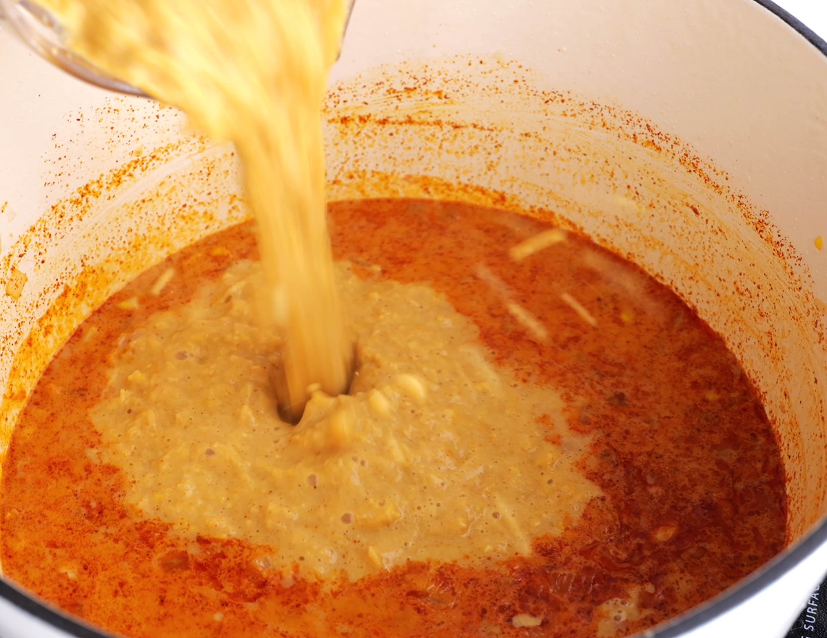 Pouring blended soup mixture into the pot with the rest of the soup.