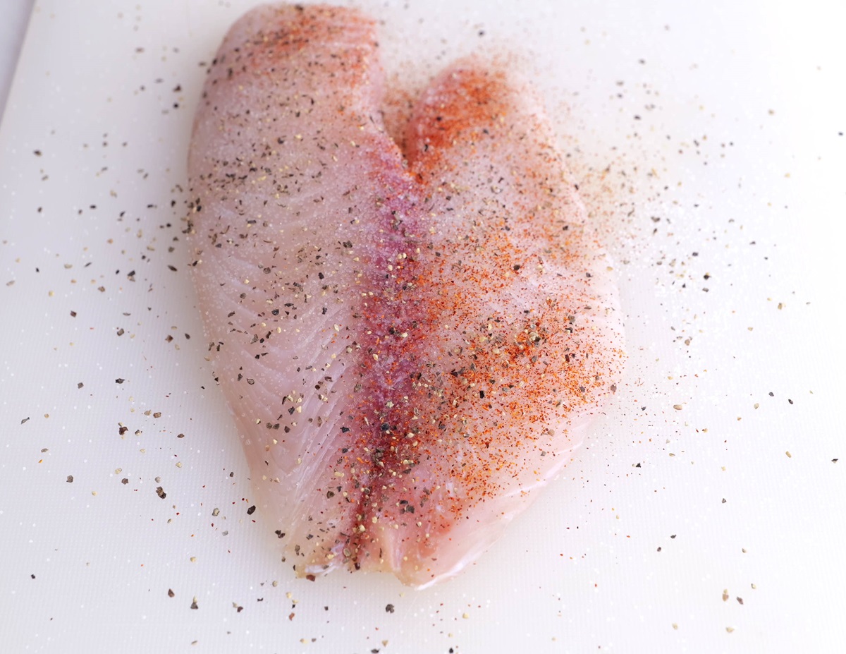 Sole filet on a cutting board, sprinkled with salt, pepper, and paprika.