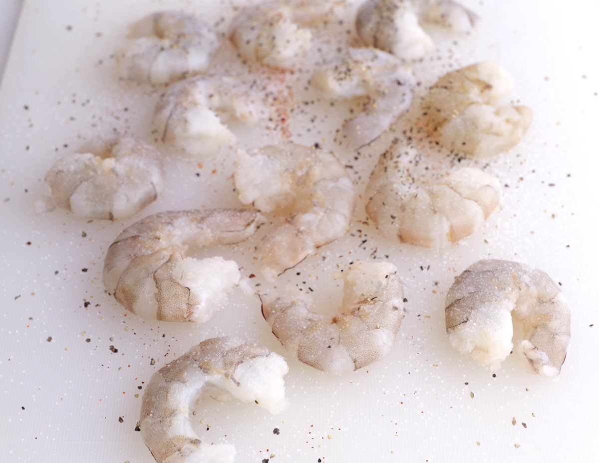 Raw shrimp on a cutting board sprinkled with salt and pepper.