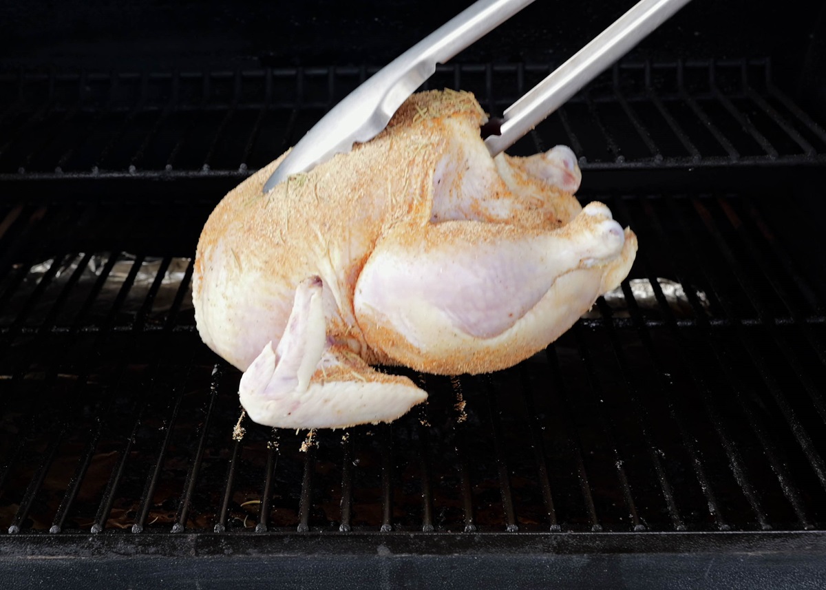 Tongs placing chicken on a smoker grill