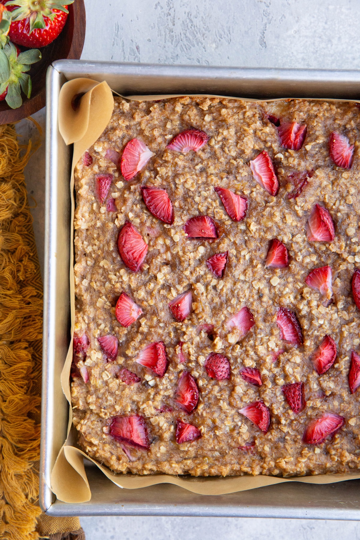 Strawberry breakfast bars, fresh out of the oven with a golden napkin and a bowl of fresh strawberries to the side.
