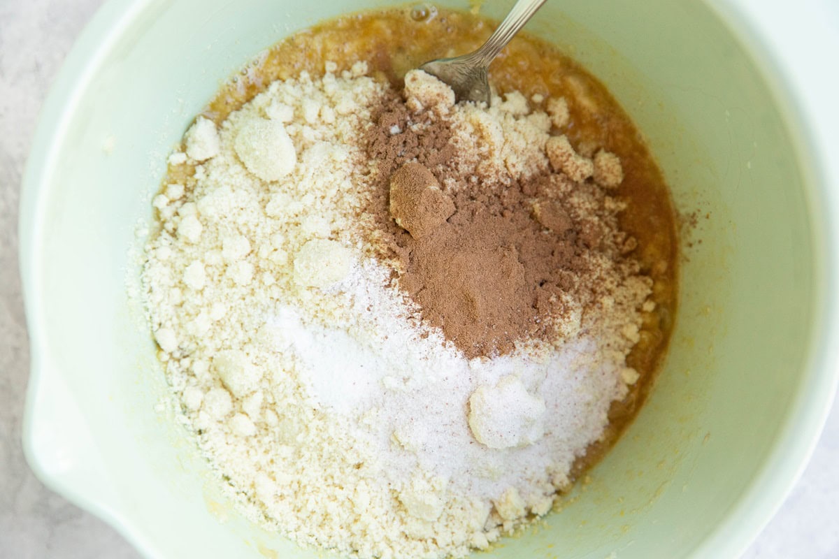 Almond flour, baking powder, cinnamon and salt on top of wet ingredients in a mixing bowl to make cookie dough.