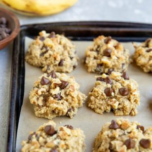 Almond flour banana cookies on a baking sheet with bananas in the background, fresh out of the oven and ready to serve.