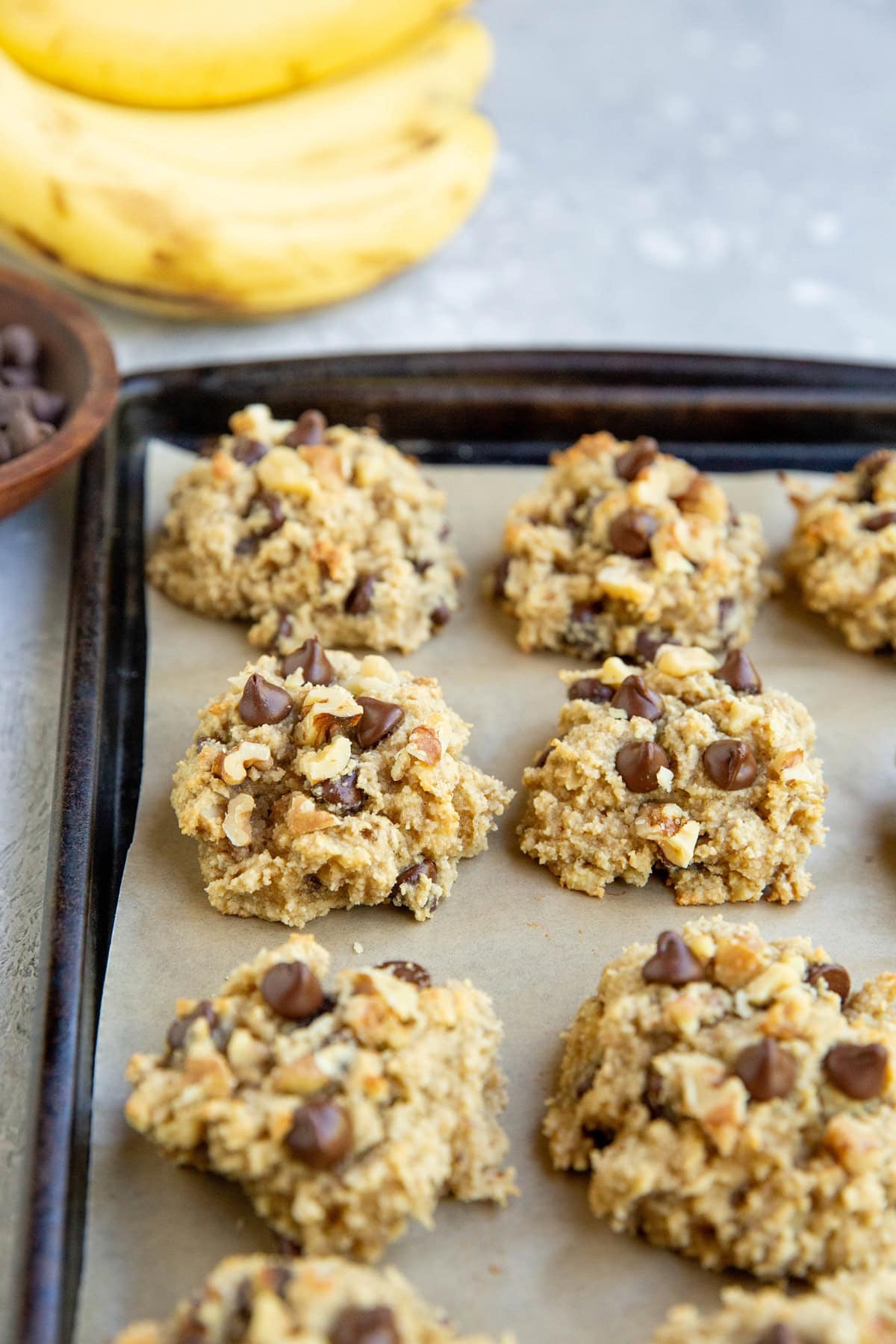 Almond flour banana cookies on a baking sheet with bananas in the background, fresh out of the oven and ready to serve.