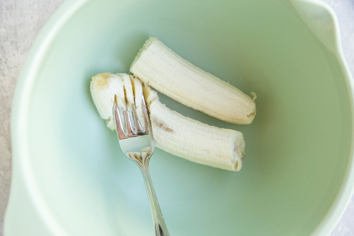 Fork mashing a banana in a mixing bowl.