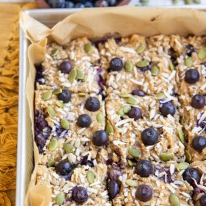 Baking dish of blueberry breakfast bars sprinkled with seeds and coconut.