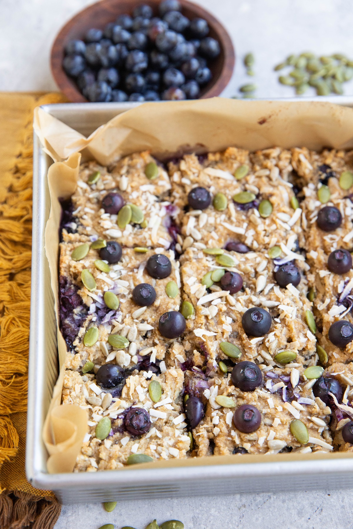 Baking dish of blueberry breakfast bars sprinkled with seeds and coconut.