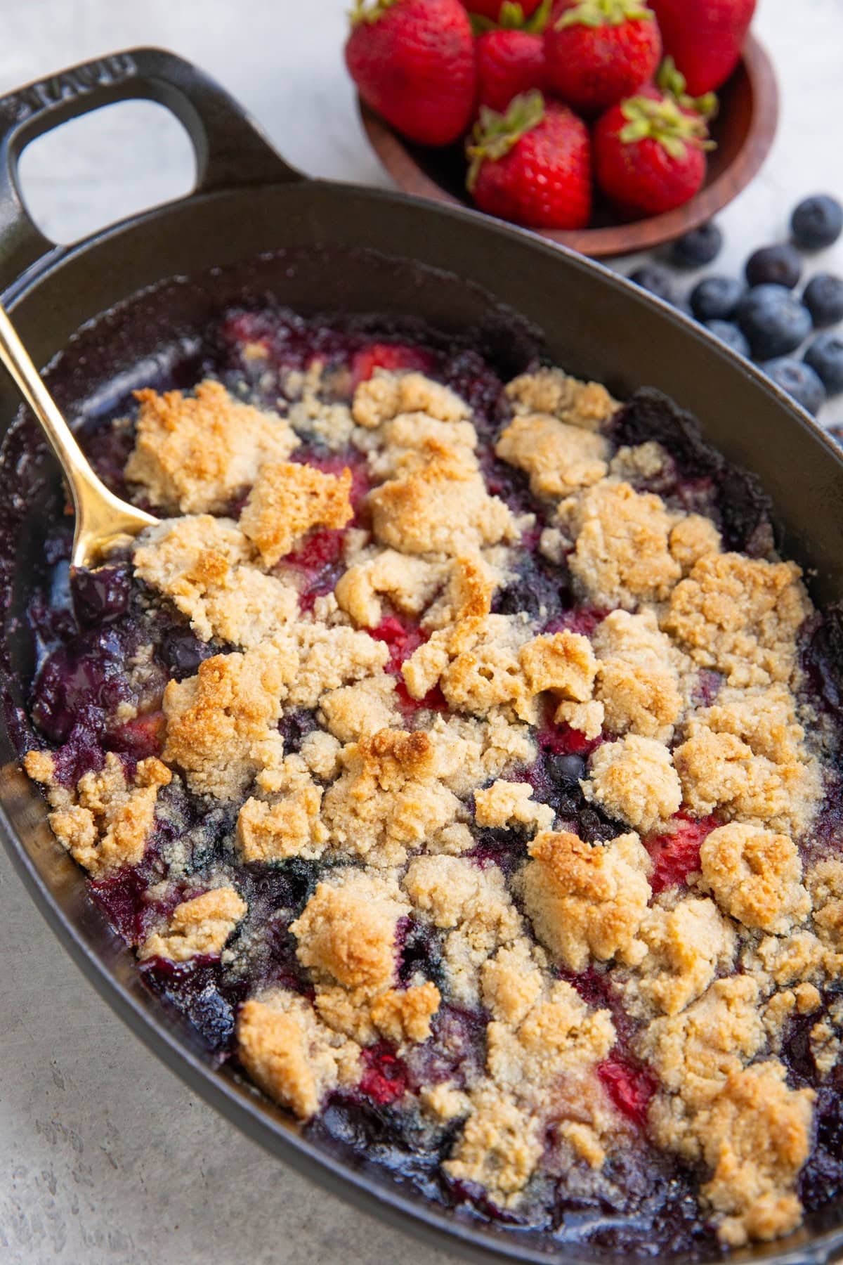 Baking dish of mixed berry crisp fresh out of the oven with fresh berries in the background.