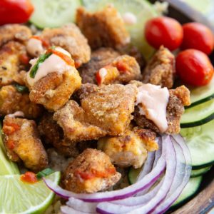 Crispy chicken in a bowl with fresh vegetables and sauce.