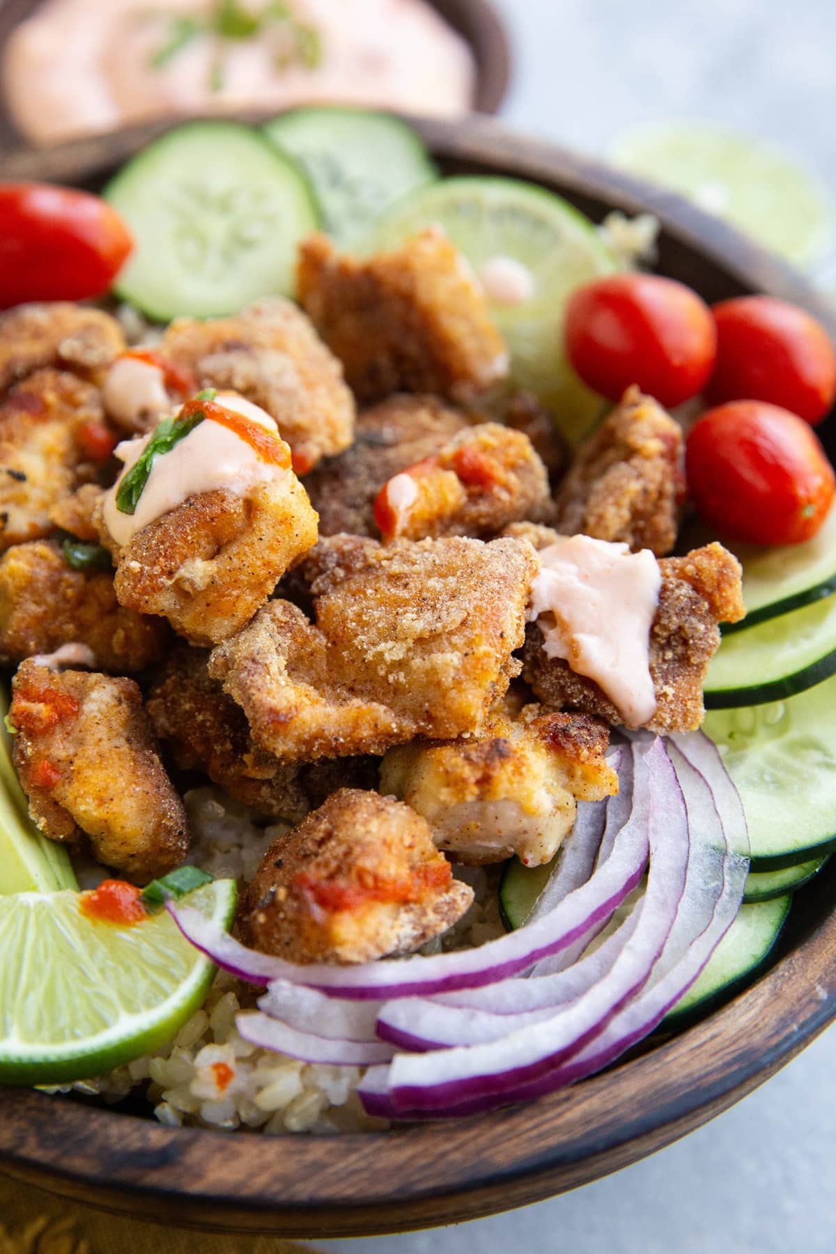 Crispy chicken in a bowl with fresh vegetables and sauce.