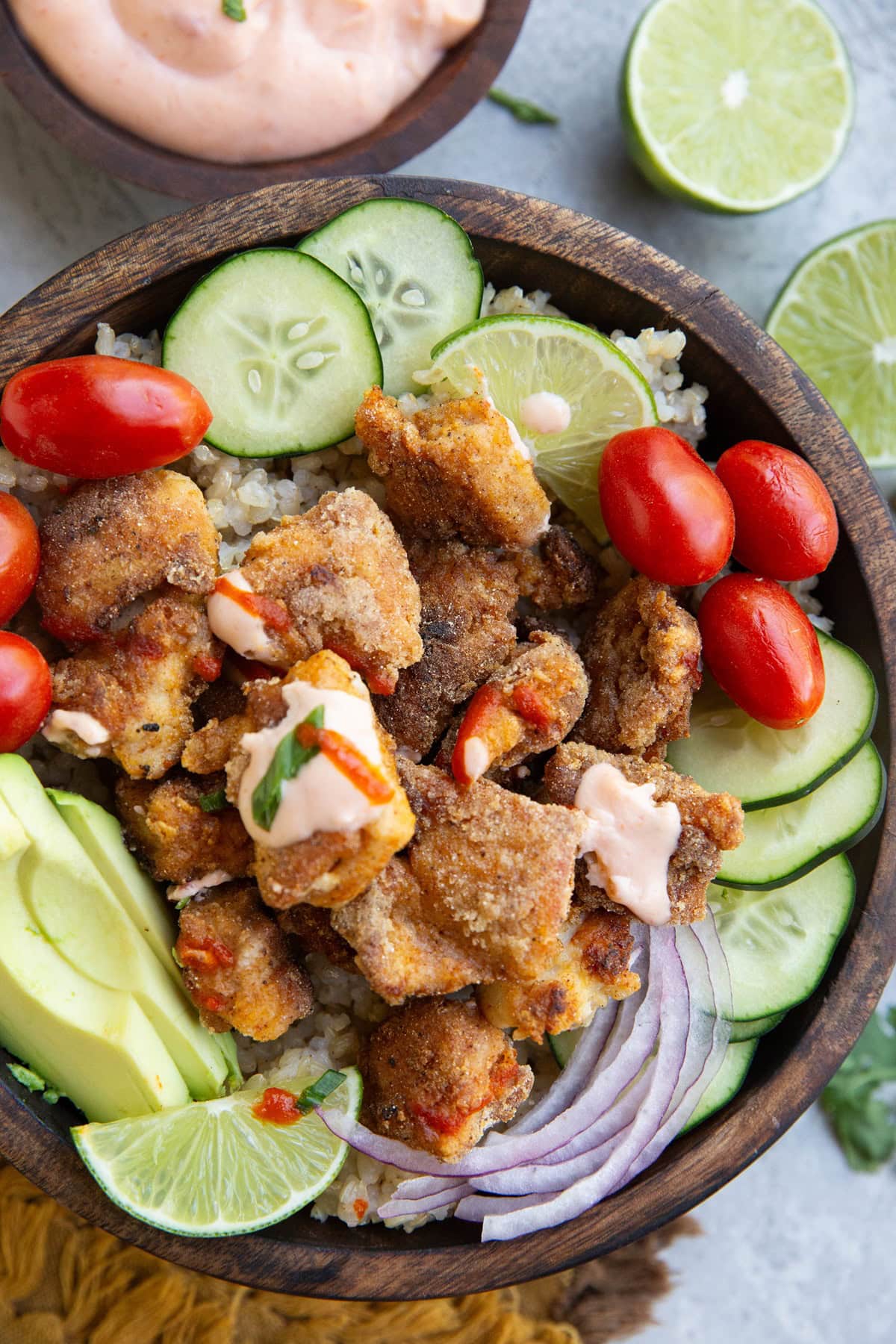 Big wooden bowl of pan fried chicken with rice and vegetables drizzled with sauce.