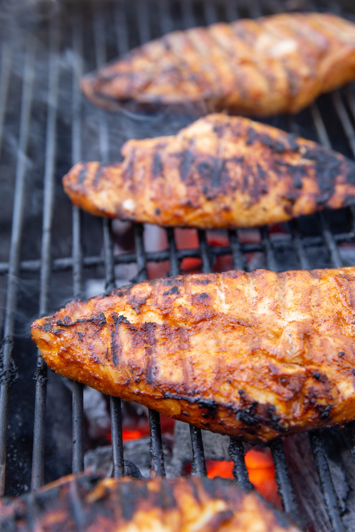 Chicken breasts grilling on a charcoal grill with coals below the grill grate.