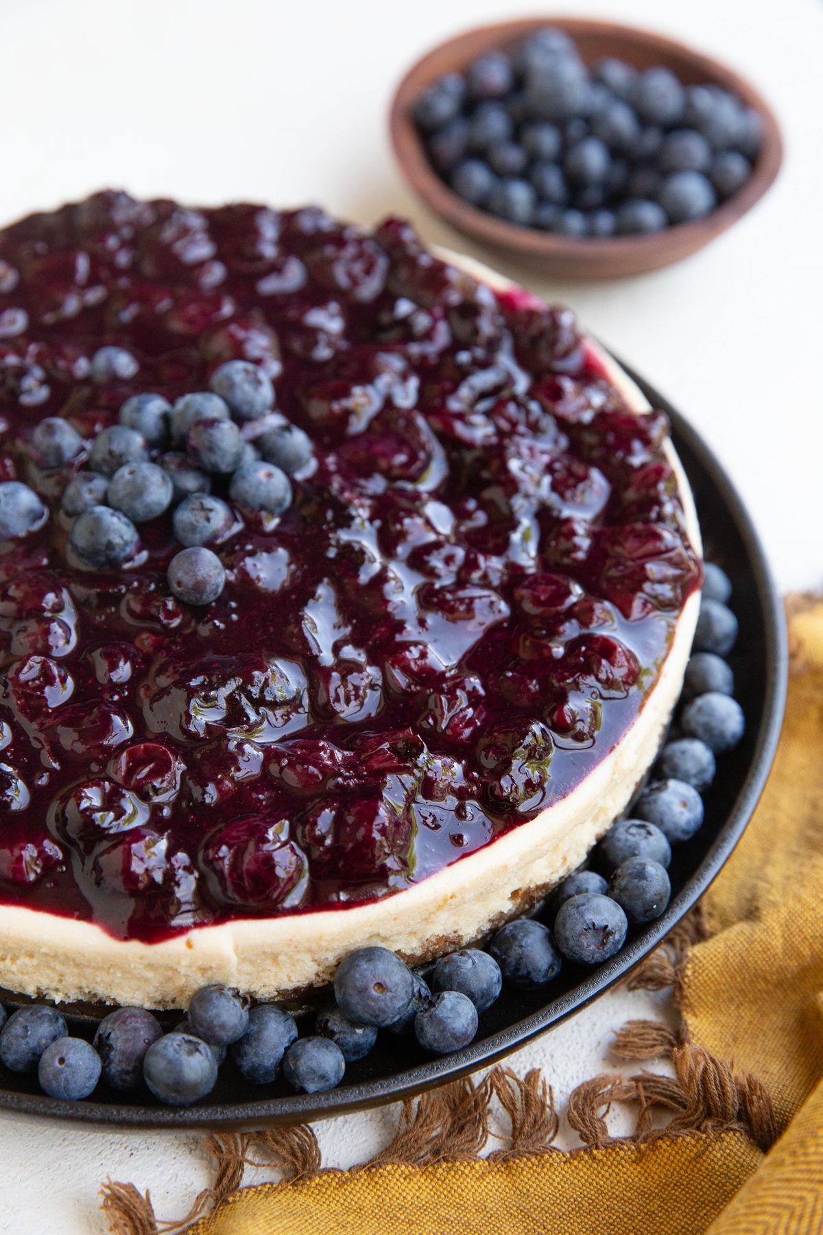 Whole cheesecake with blueberry topping and a bowl of fresh blueberries in the background, ready to serve.