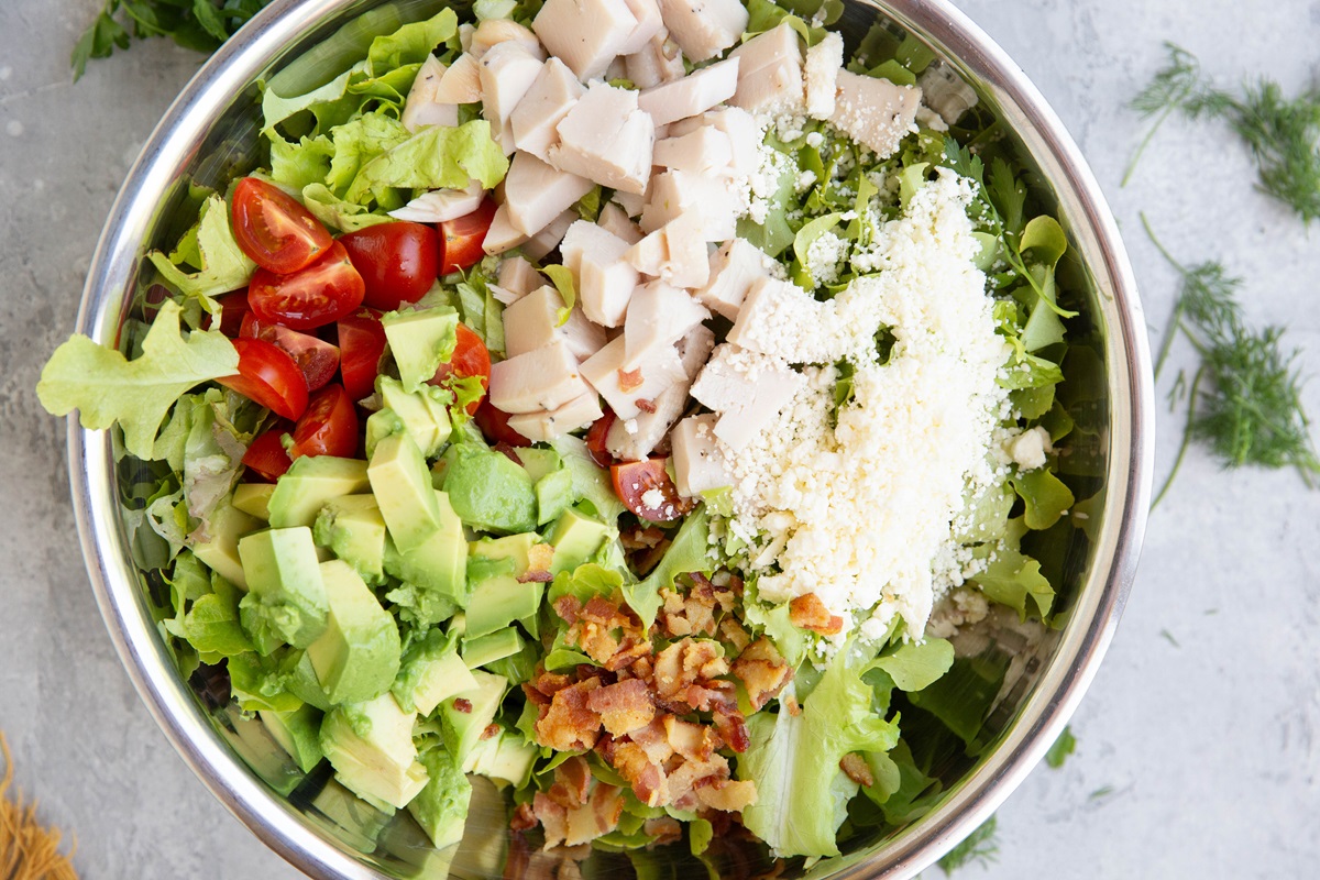Stainless steel bowl of salad ingredients, ready to be tossed with dressing.