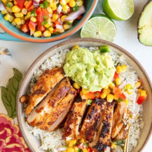 Burrito bowl with cilantro lime rice, guacamole, corn salsa, and chipotle chicken with a bowl of corn salsa to the side.