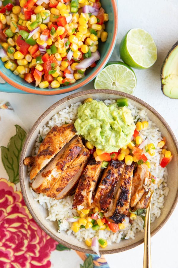 Burrito bowl with cilantro lime rice, guacamole, corn salsa, and chipotle chicken with a bowl of corn salsa to the side.