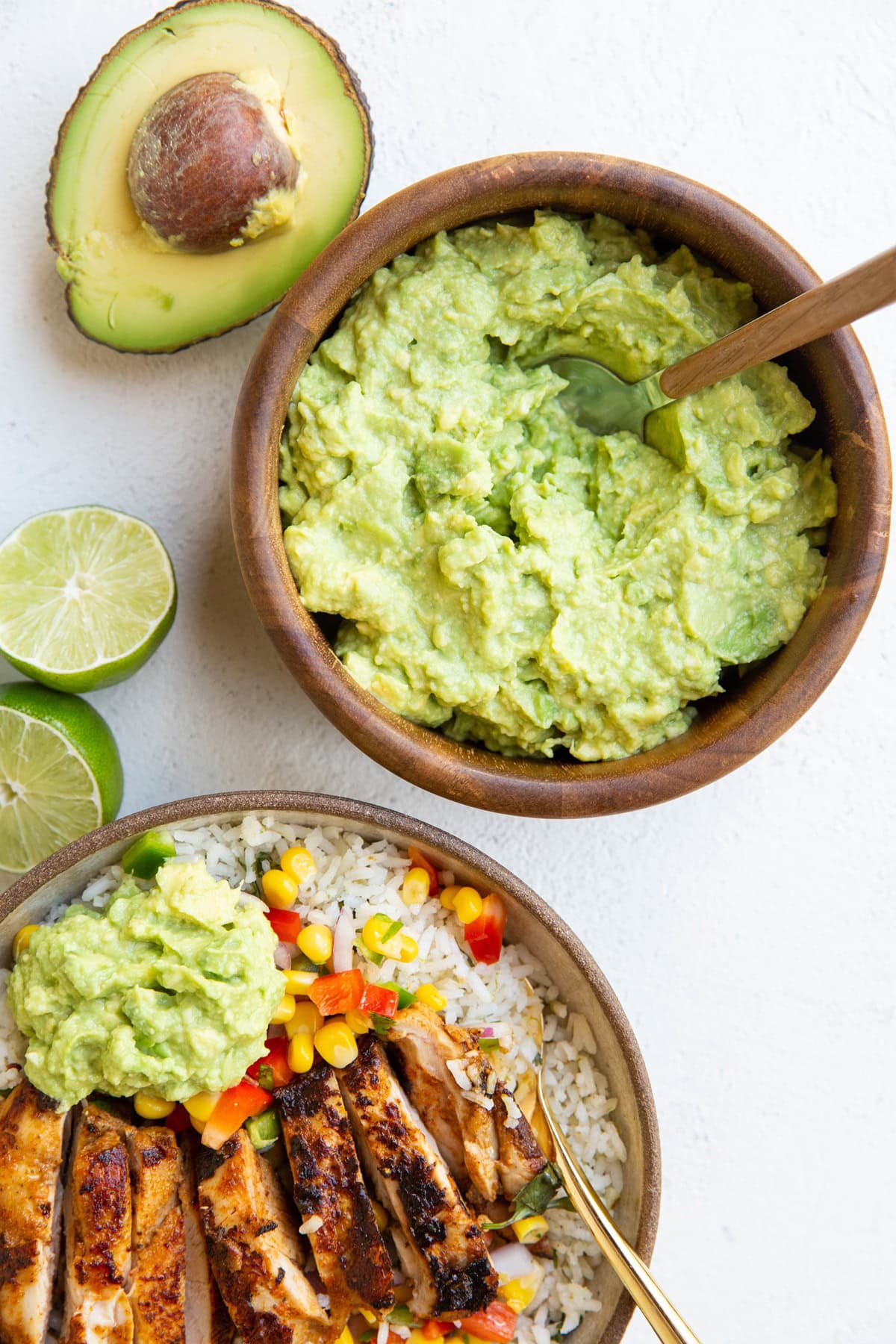 Wooden bowl of guacamole and a burrito bowl with chicken, rice, corn salsa and guac.