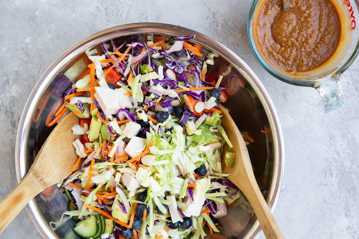 Salad ingredients in a stainless steel bowl and peanut dressing to the side, ready to toss together.