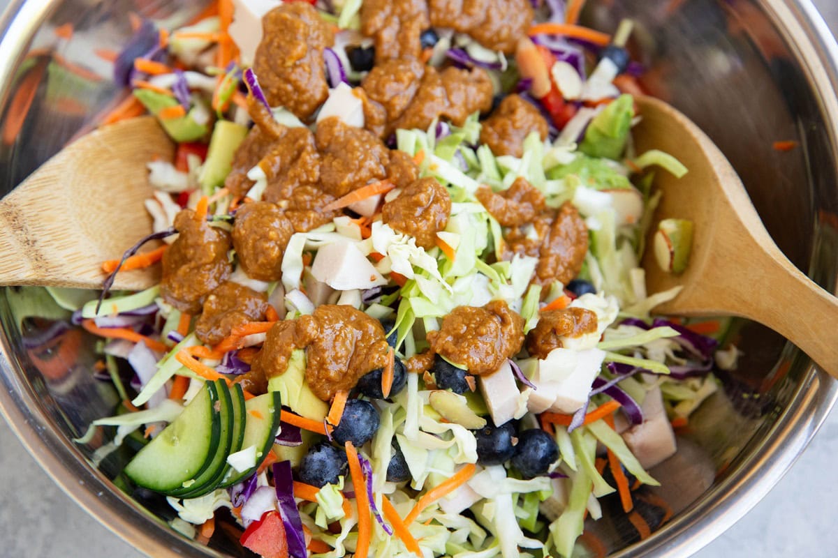 Peanut dressing on top of salad in a large mixing bowl.