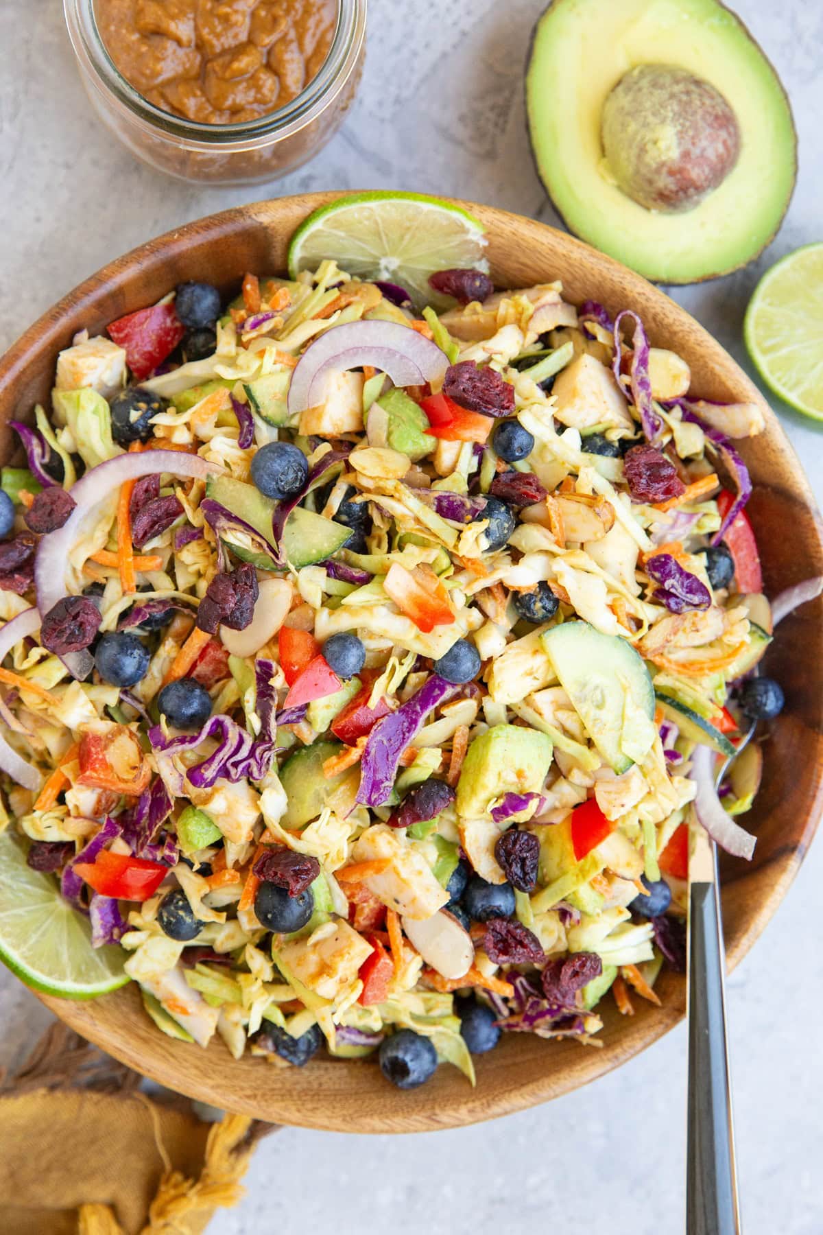 Wooden bowl of cabbage salad with peanut dressing to the side and half an avocado and lime. Ready to serve.