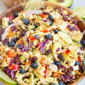 Big salad bowl with cabbage salad inside. Jar of peanut dressing and avocado in the background.