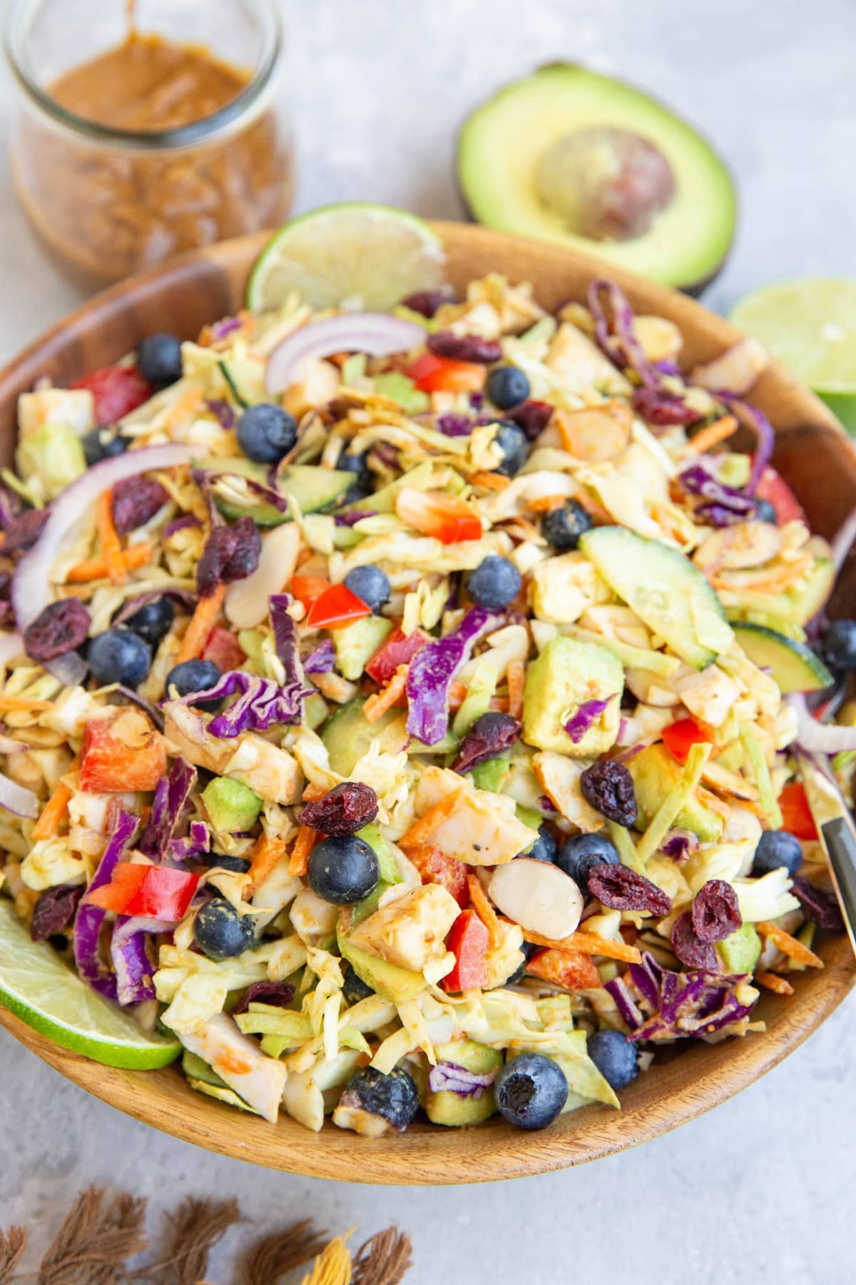 Big salad bowl with cabbage salad inside. Jar of peanut dressing and avocado in the background.