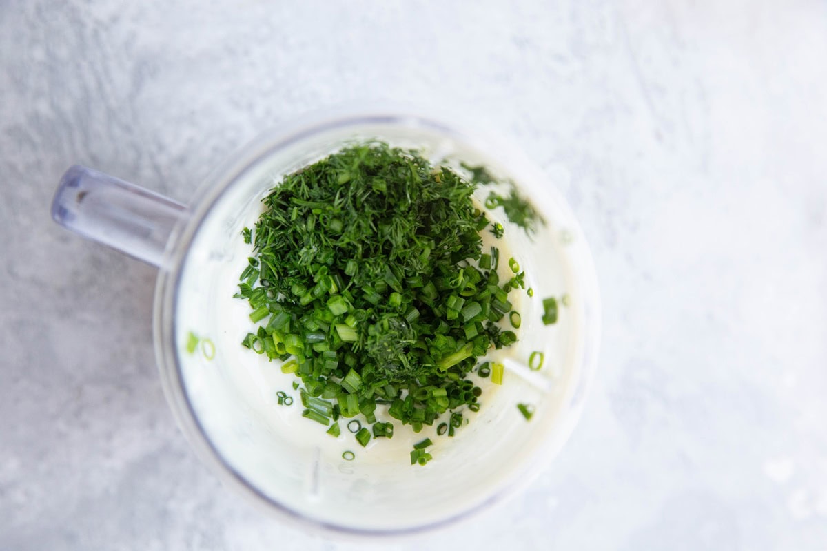 Fresh herbs on top of creamy dressing, ready to be mixed in.