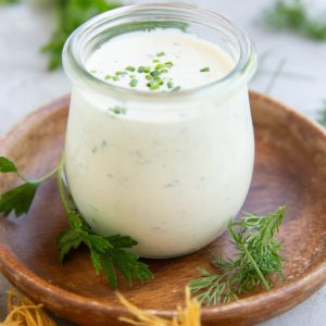 Jar full of homemade ranch dressing with fresh herbs all around.