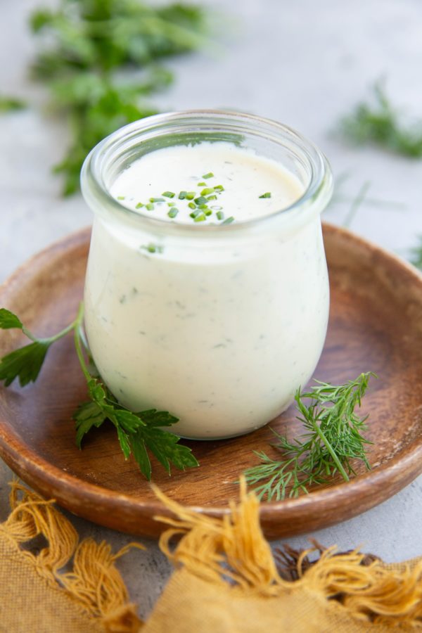 Jar full of homemade ranch dressing with fresh herbs all around.