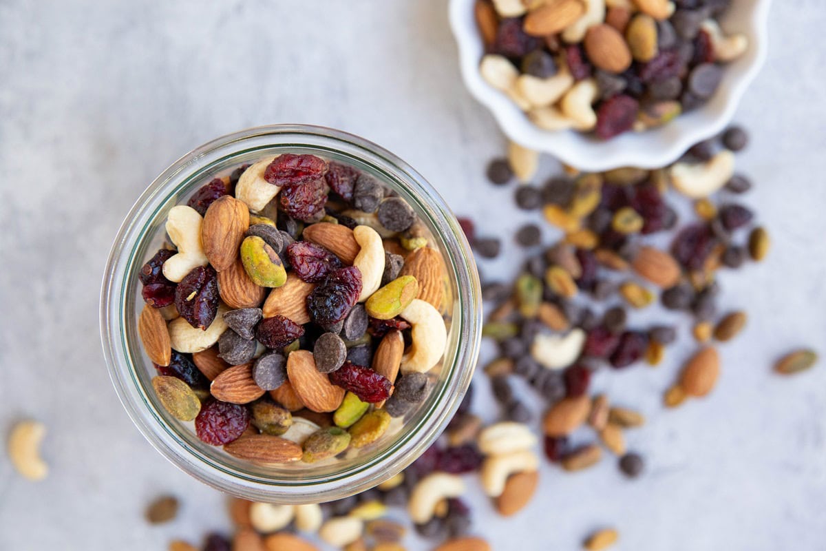 Glass jar of trail mix with a bowl of trail mix to the side.