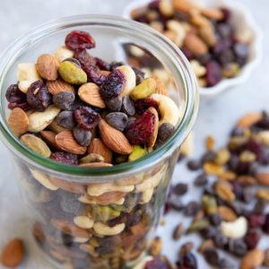 Glass jar of trail mix with trail mix scattered about.