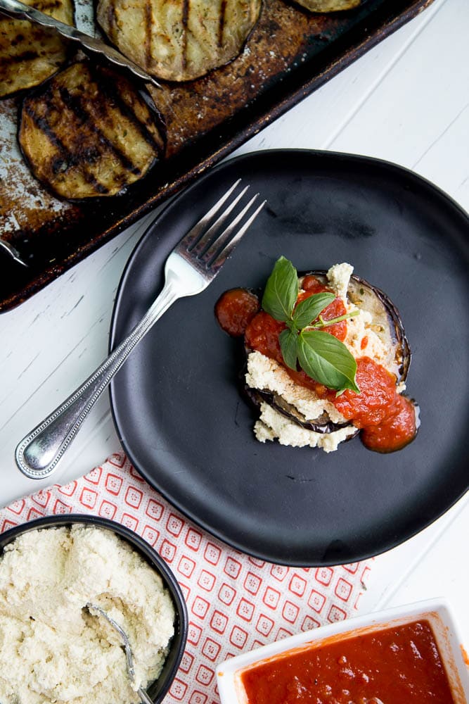 Stack of grilled eggplant with cheese and sauce on a plate.