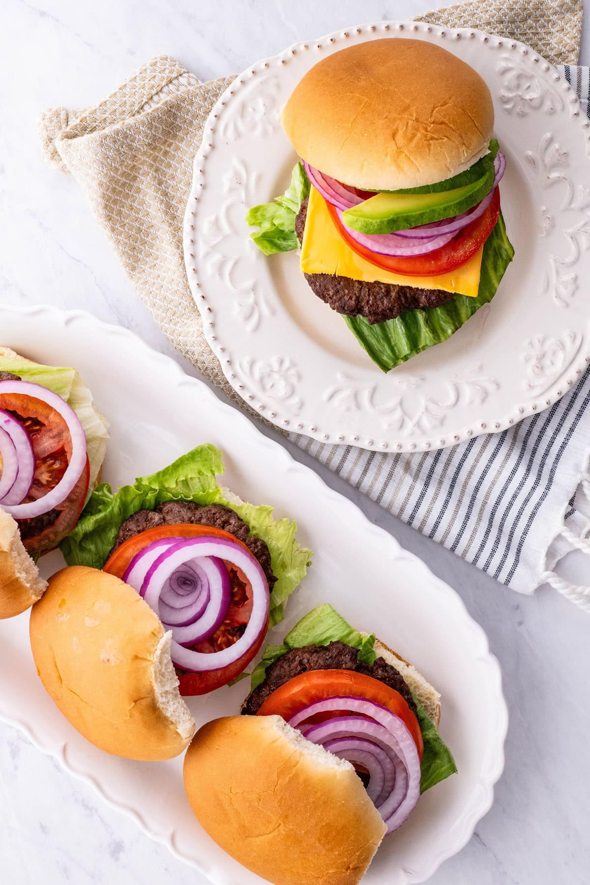 Two plates with burgers on top, ready to serve. Napkins to the side.