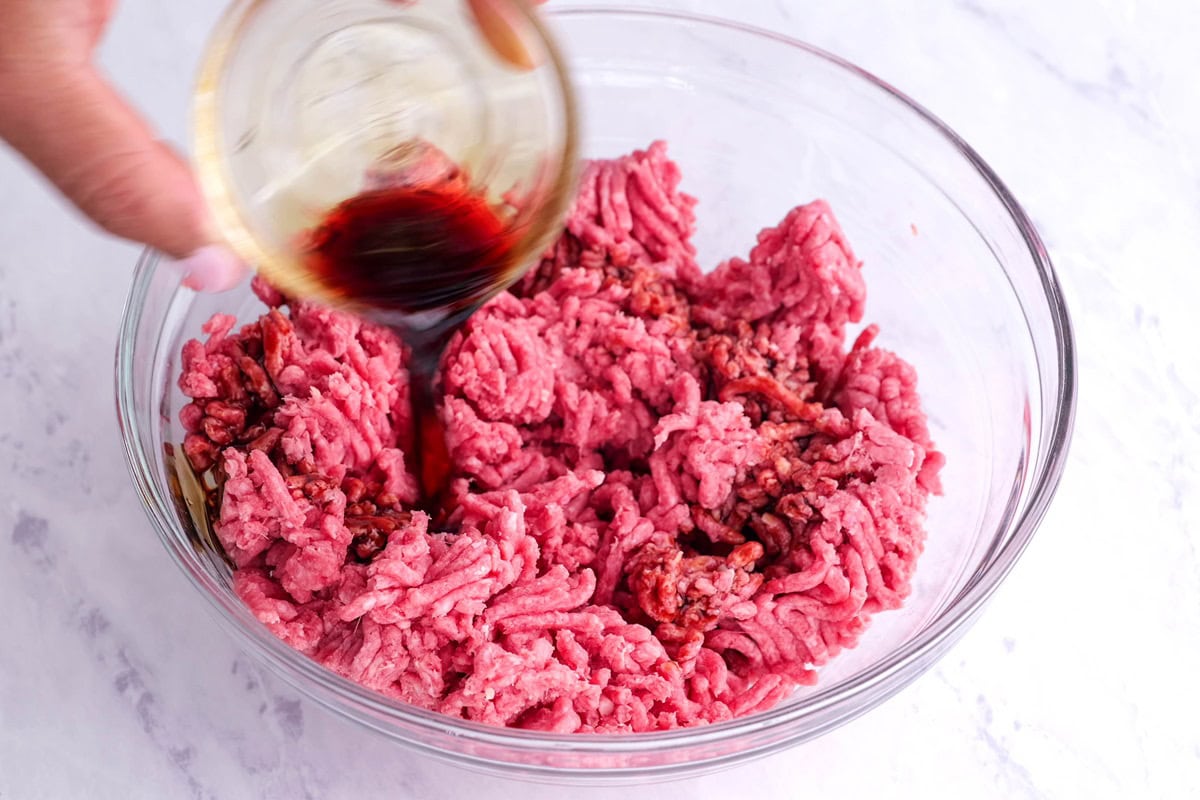 Pouring soy sauce into a mixing bowl with ground beef.