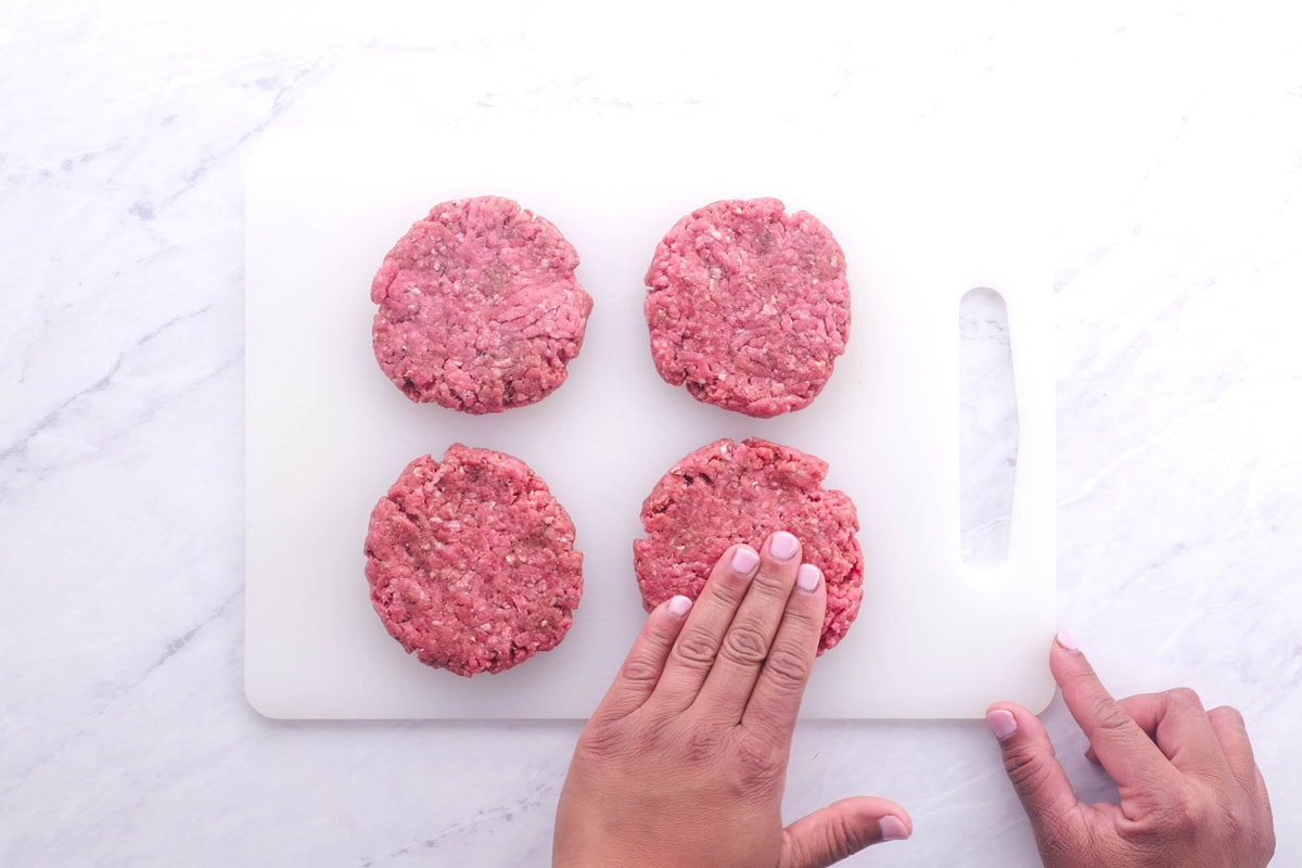 Cutting board with four beef patties on top and hands forming the patties. Ready to cook.