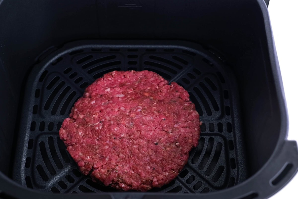 Beef burger patty in an air fryer basket, ready to air fry.